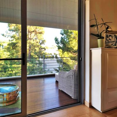 Fliegengitterplissee geschlossen am Balkon. Wald dahinter erkennbar