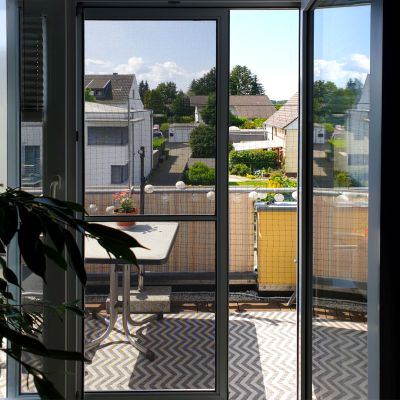 Fliegengitterschiebetür von innen betrachtet. Leicht geöffnet. Dahinter ein Balkon