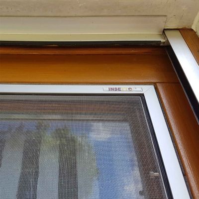 Fliegengitterrahmen in weiß an einem Holzfenster. Es spiegelt sich im Fenster die Umgebung