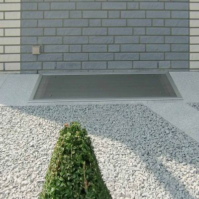 Lichtschachtabdeckung neben einem Steingarten