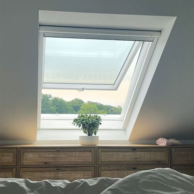 Fliegengitterrollo am Dachfenster. Fenster geöffnet, im Hintergrund ein Wald