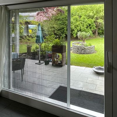 Fliegengitterplissee sehr breit an Terrassentür, draußen ein Garten