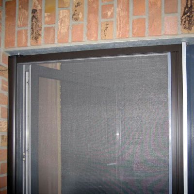 Braunes Fliegengitterrollo an Tür - Backsteinwände daneben